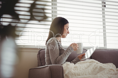 Side view of woman using tablet while drinking coffee