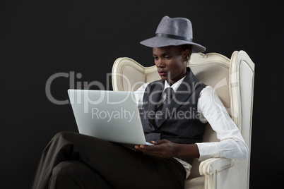 Androgynous man using laptop while sitting on a chair