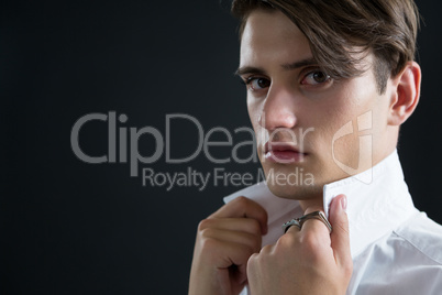 Androgynous man holding his collar against black background