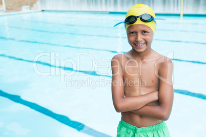 Smiling boy standing with arms crossed near poolside