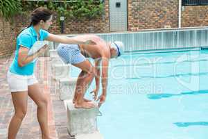 Swim coach assisting senior man in swimming