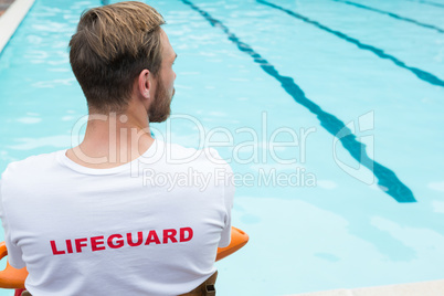 Lifeguard sitting on chair with rescue buoy at poolside