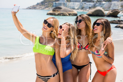 Female friends in bikinis taking selfie at beach