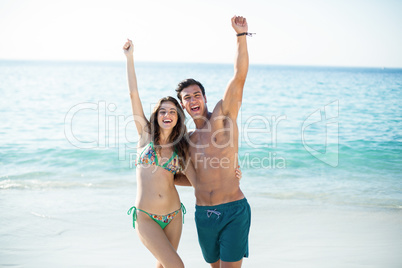 Couple standing with arms raised at beach