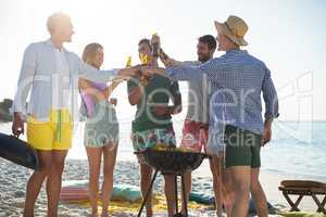 Friends toasting while standing by barbecue at beach