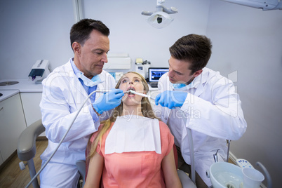 Dentists examining a female patient with tools