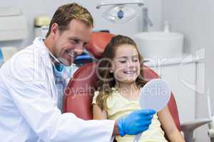 Dentist showing mirror to young patient in dental clinic