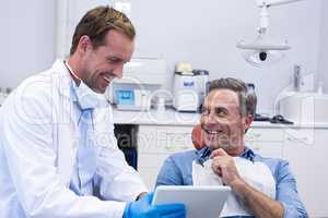 Dentist discussing over digital tablet with male patient