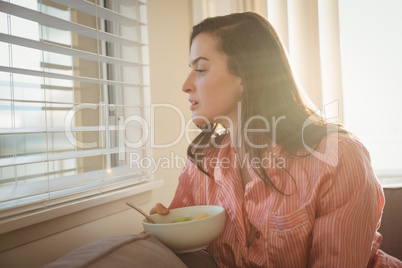 Woman looking through window while sitting on sofa
