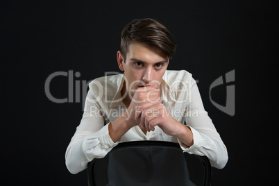 Androgynous man sitting on chair with hand on his chin