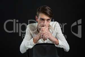 Androgynous man sitting on chair with hand on his chin