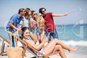 Woman listening music while friends taking selfie at beach
