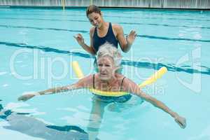 Female coach helping senior woman in swimming pool