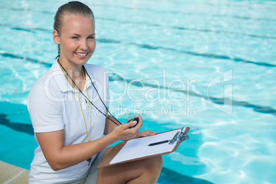 Smiling swim coach holding clipboard and stopwatch at poolside