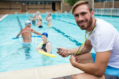 Smiling swim coach holding stopwatch near poolside