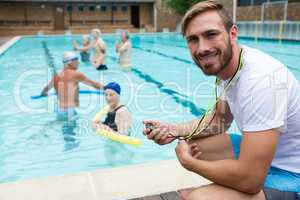 Smiling swim coach holding stopwatch near poolside