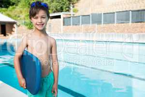 Smiling boy holding kickboard at poolside