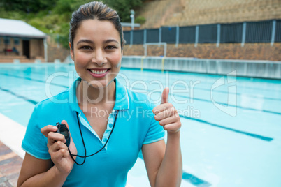 Portrait of swim coach holding stopwatch and showing thumbs up near poolside