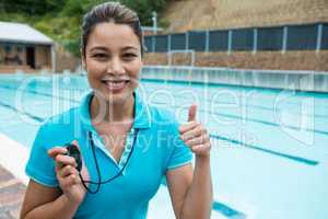 Portrait of swim coach holding stopwatch and showing thumbs up near poolside