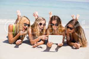 Female friends in bikinis smiling while looking in digital tablet