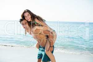 Boyfriend piggybacking girlfriend on shore at beach