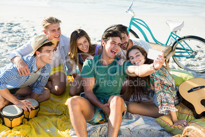 Friends taking selfie while sitting at beach