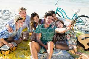Friends taking selfie while sitting at beach