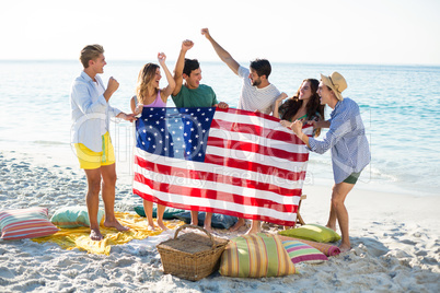 Friends holding American flag on shore at beach