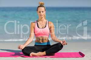 Woman meditating in lotus position on shore at beach