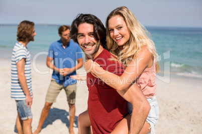 Boyfriend piggybacking girlfriend by friends at beach