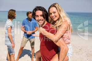 Boyfriend piggybacking girlfriend by friends at beach