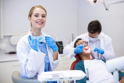 Portrait of smiling dentist standing while her colleague examining patient in background