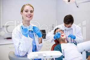 Portrait of smiling dentist standing while her colleague examining patient in background