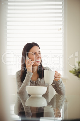 Smiling woman talking on mobile phone while eating breakfast