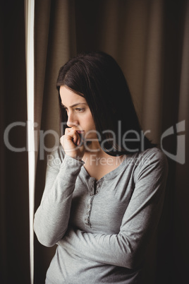 Thoughtful woman standing against curtain