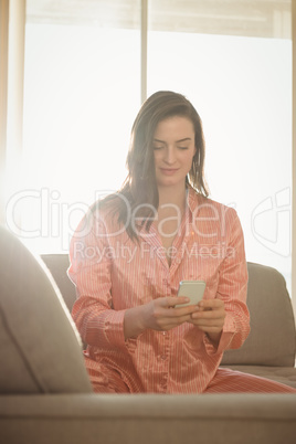 Woman in night dress using smart phone while sitting on sofa