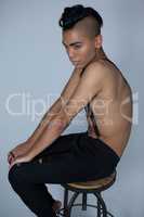 Transgender wearing suspenders sitting on stool