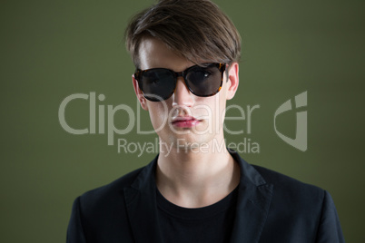 Androgynous man in sunglasses posing against green background