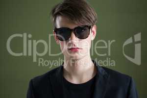 Androgynous man in sunglasses posing against green background