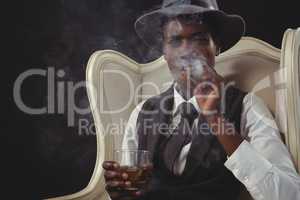 Androgynous man smoking cigar while while sitting on a chair