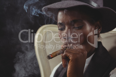 Androgynous man smoking cigar while sitting on a chair