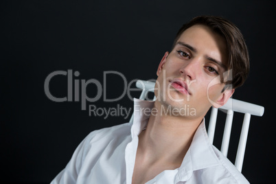 Androgynous man posing while sitting on chair
