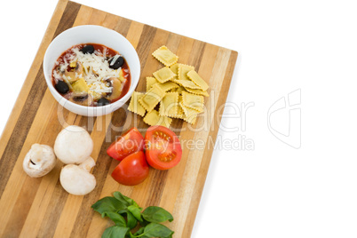 Food in bowl by ravioli and vegetables on cutting board