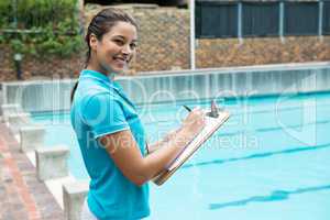 Smiling female coach writing on clipboard