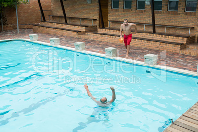 Lifeguard jumping into a swimming pool to rescue drowning senior man