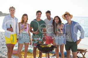 Friends having drinks by barbecue at beach