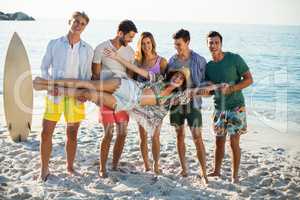 Friends holding young woman while standing on shore at beach