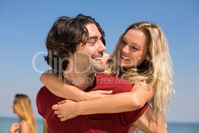 Boyfriend piggybacking girlfriend at beach against sky