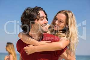 Boyfriend piggybacking girlfriend at beach against sky