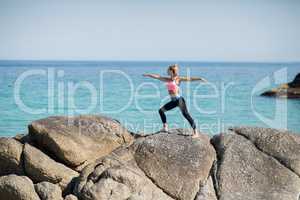 Woman practicing warrior pose on rocky shore